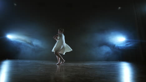Zoom-camera-moves-around-the-stage-with-software-and-smoke.-Girl-ballerina-dancing-in-a-white-dress-spinning-plastic-while-performing-pirouettes-and-rotations-experiencing-emotions-and-dramatic-atmosphere.